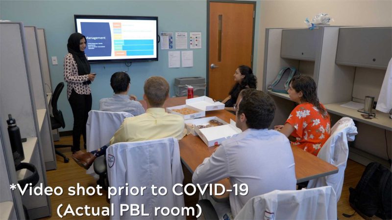 One student presenting at the large screen and five students sit around the table. Image was taken prior to COVID. 