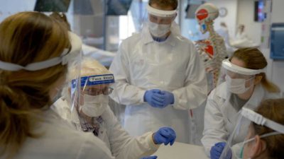 A faculty member and four students, all wearing masks, face shields, and additional PPE (personal protective equipment) during an anatomy class.