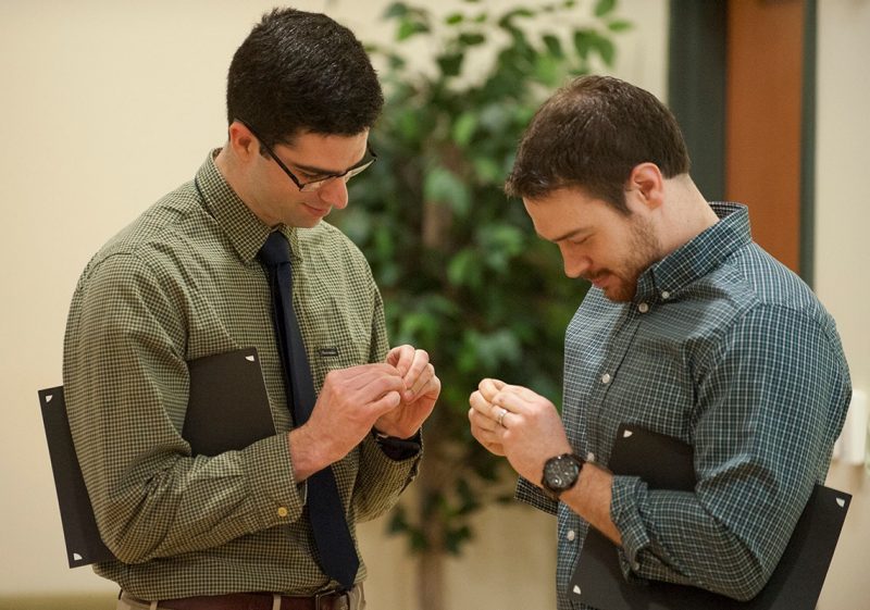 Michael Gallager (left) and Nathan Johnson work to open pins they received as part of the Gold Humanism Honor Society induction ceremony.