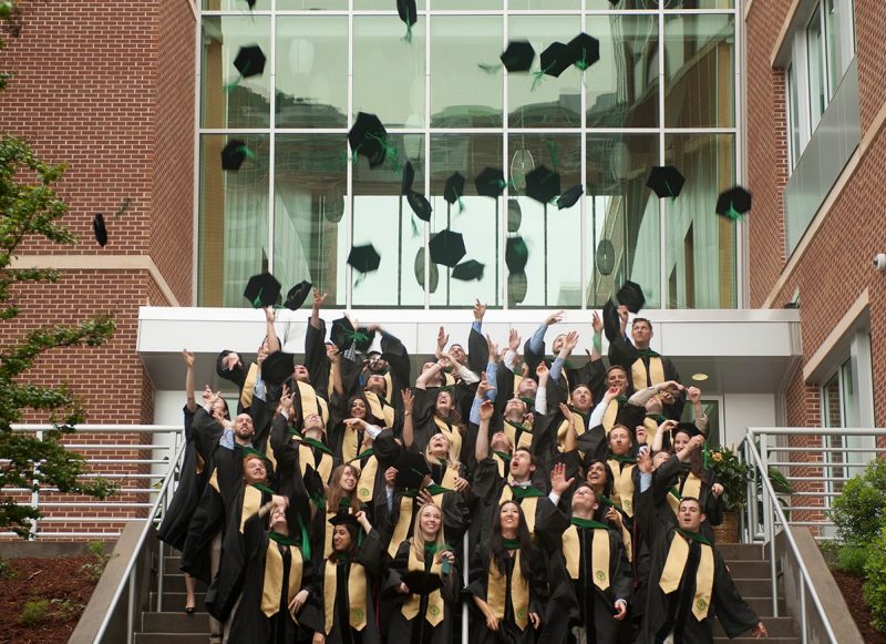 First graduating class throw their hats in the air in front of the Virginia Tech Carilion School of Medicine building.