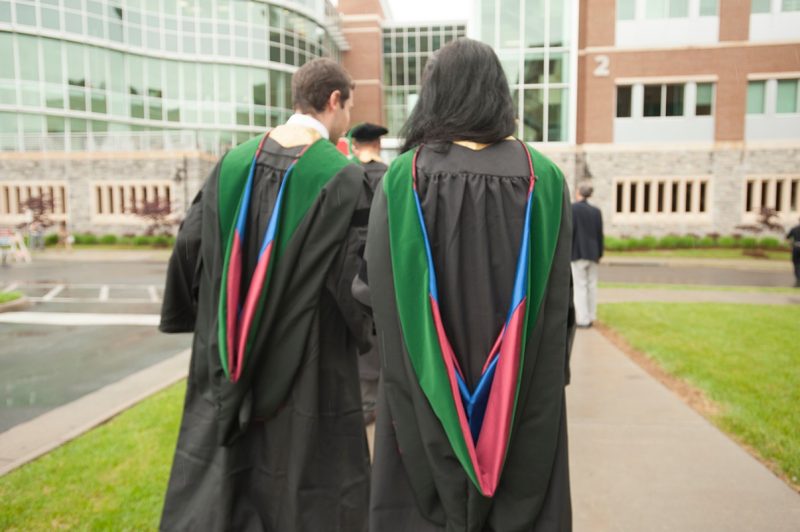 Two students walking away from the camera towards the School of Medicine, wearing the custom designed hoods