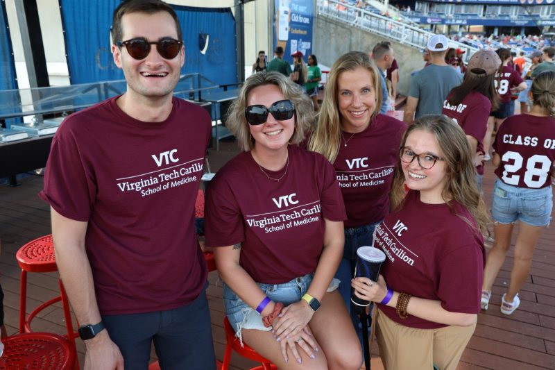 Four students wearing maroon VTCSOM t-shirts at an outdoor event.