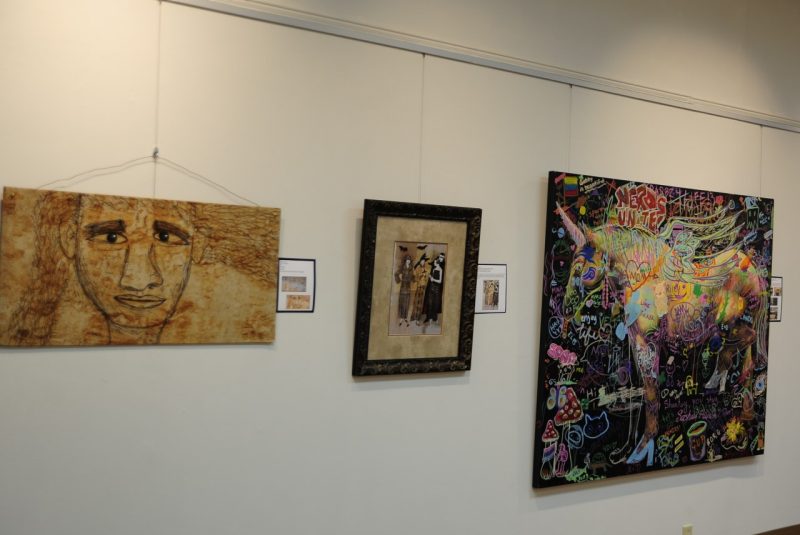 Three works of art (paintings) hanging side by side in a gallery