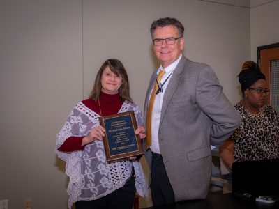 Woman holding award plaque stadning next to a man, both smiling