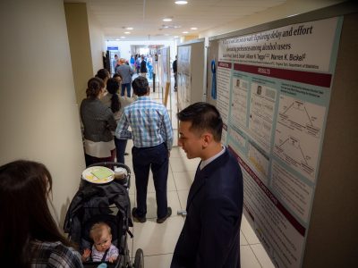 Man, woman, and baby in stroller in front of scientific poster