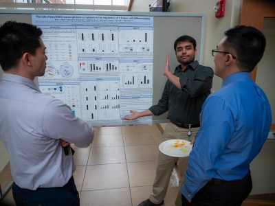 Three men discussing a scientific poster