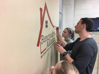 three volunteers painting the renovation alliance logo on the wall