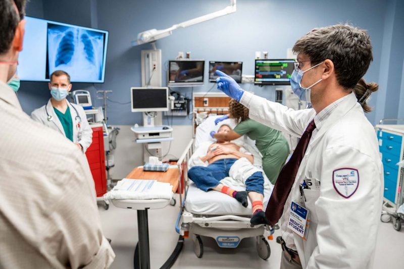 Medical school student Michael Spinosa points to a chest X-ray image while other students tend to a patient during an emergency simulation.