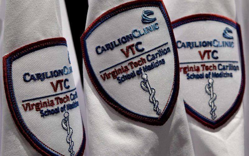 Three white coat sleeves with patches containing Carilion Clinic and VTCSOM logos