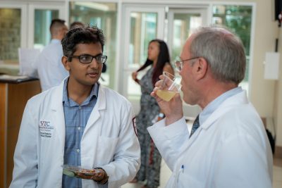 Medical student Varun Kavuru wearing white coat speaking with physician at a reception.