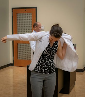 Medical Student Alyssa Wenzel puts on her white coat at the front of an auditorium.