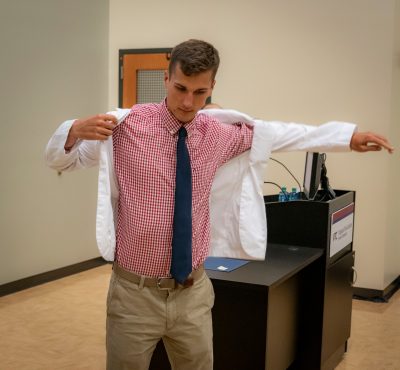 Medical student Parker Hambright puts on his white coat in the front of an auditorium