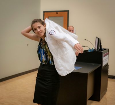 Medical Student Keri Godbe puts on her white coat in the front of an auditorium.