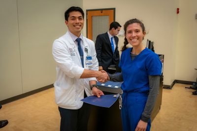 Medical student Jean Sabile shaking the hand of a woman. Student at podium in background.