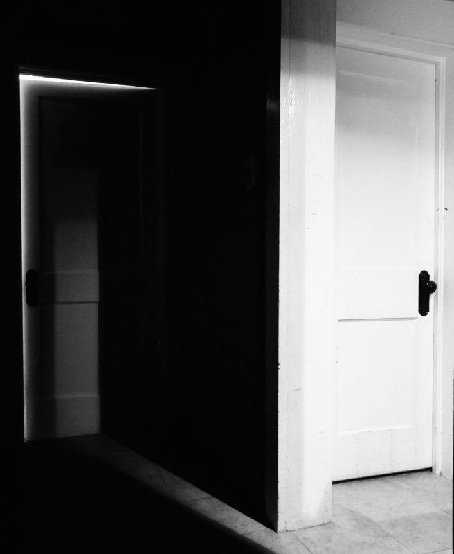 A photo of two doors divided by a wall. The door on the left is in the shadows, the door on the right is bright white