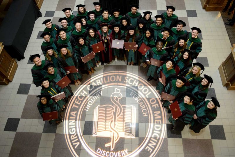Aerial view of graduates in full regalia encircling the VTCSOM seal projected onto the floor