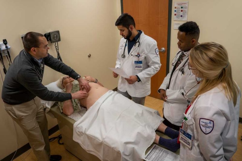 Instructor demonstrating a procedure with a standardized patient and three student observers