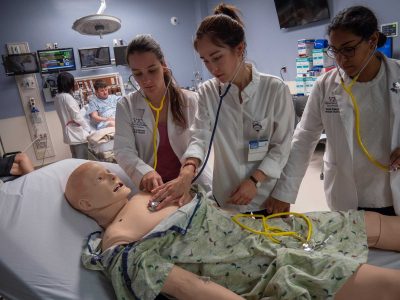 Three students taking vital signs on a simulation mannequin