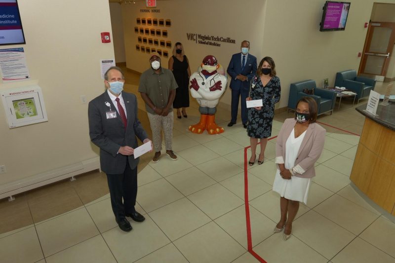 Aerial view in the VTCSOM lobby with six people lined up with the Roanoke Hokie, MD statue