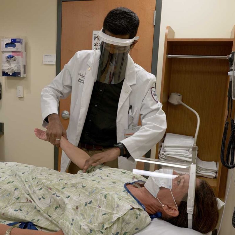 Student interacting with a standardized patient, both parties wearing protective personal equipment