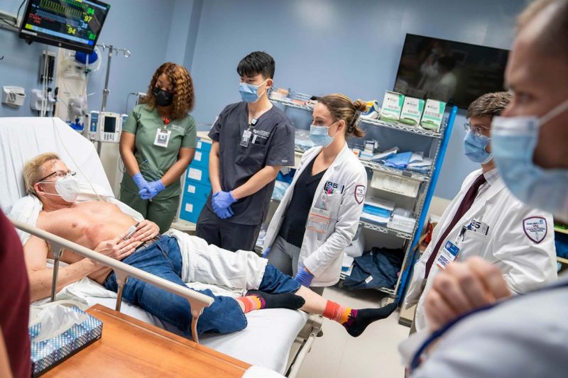 Medical school student Allison Strauss talks with a patient alongside other students during an emergency simulation.