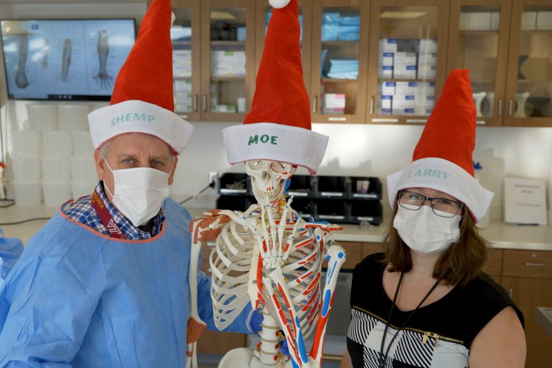 John McNamara and Emma Huston pose with a skeleton. Their hats read Shemp (John), Moe (Skeleton), and Larry (Emma)