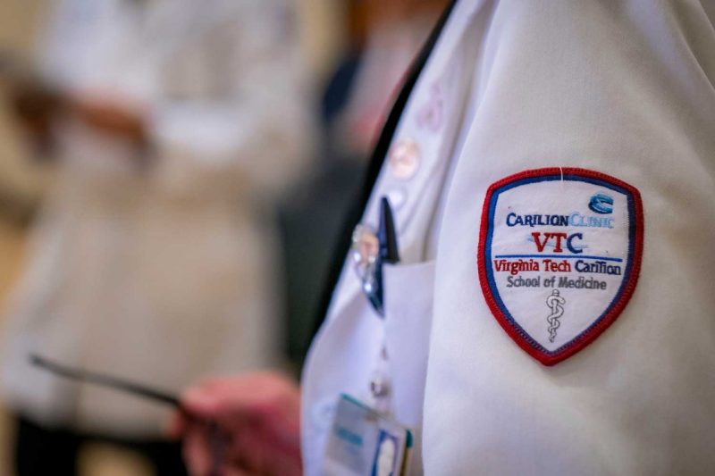 closeup of a sleeve of a VTCSOM white coat showing the patch with Carilion Clinic and VTCSOM logos