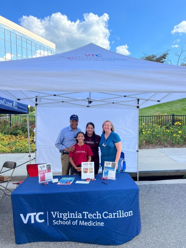 Four individuals stand behind the VTCSOM table at the Henry Street Festival.