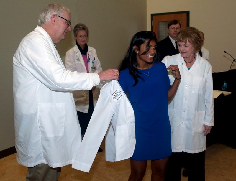 Kami Arulraja dons her white coat with the help of Founding Dean Cynda Johnson, MD and Senior Dean for Academic Affairs Daniel Harrington, MD.