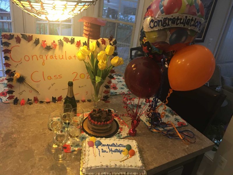 Cake with "congratulations Dr. Mustafa" accompanied by a sign with "Congratulations Class of 2020" and balloons