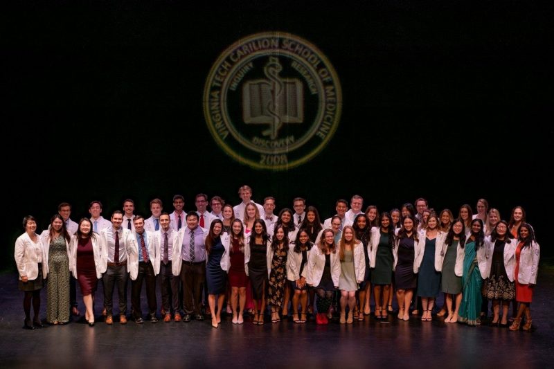 The class of 2026 line up after receiving their white coats. The VTCSOM seal is illuminated above them