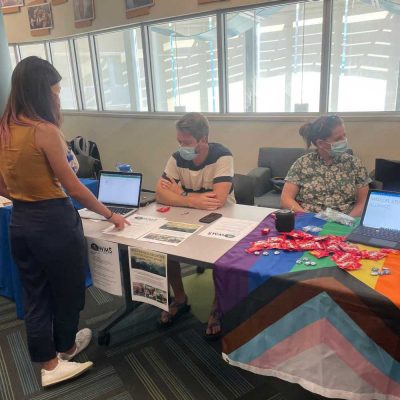a student is standing in front of the wilderness medicine interest group. The table adjacent has a pride flag with a laptop that reads Medical Student Pride Alliance