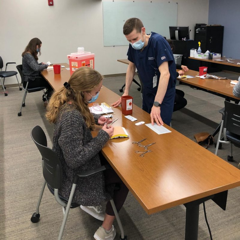Suture and biopsy workshop. Faculty mentor Josh Eikenberg oversees a student cutting a suture
